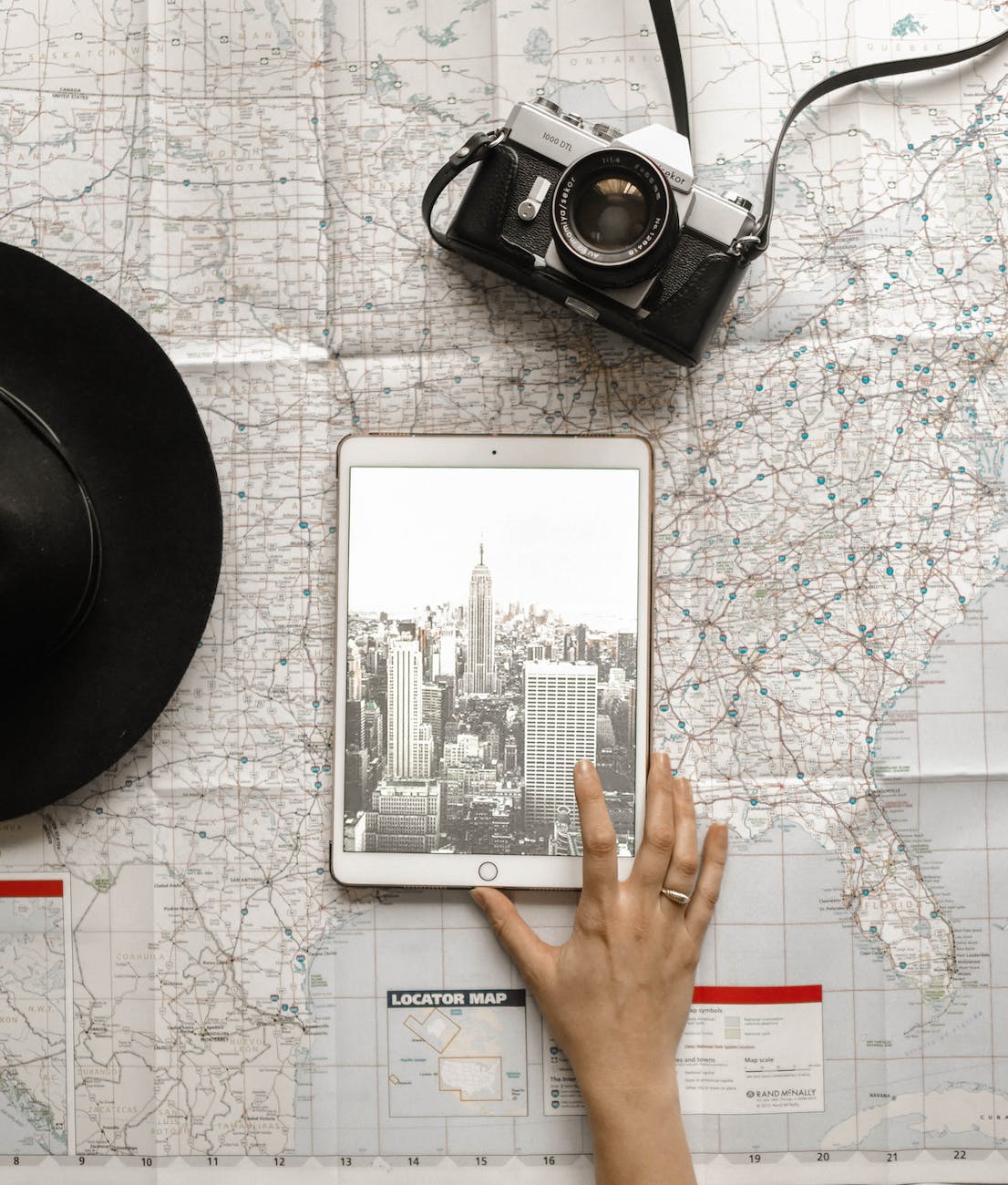 flat lay photography of person touching silver ipad on world map chart beside black hat